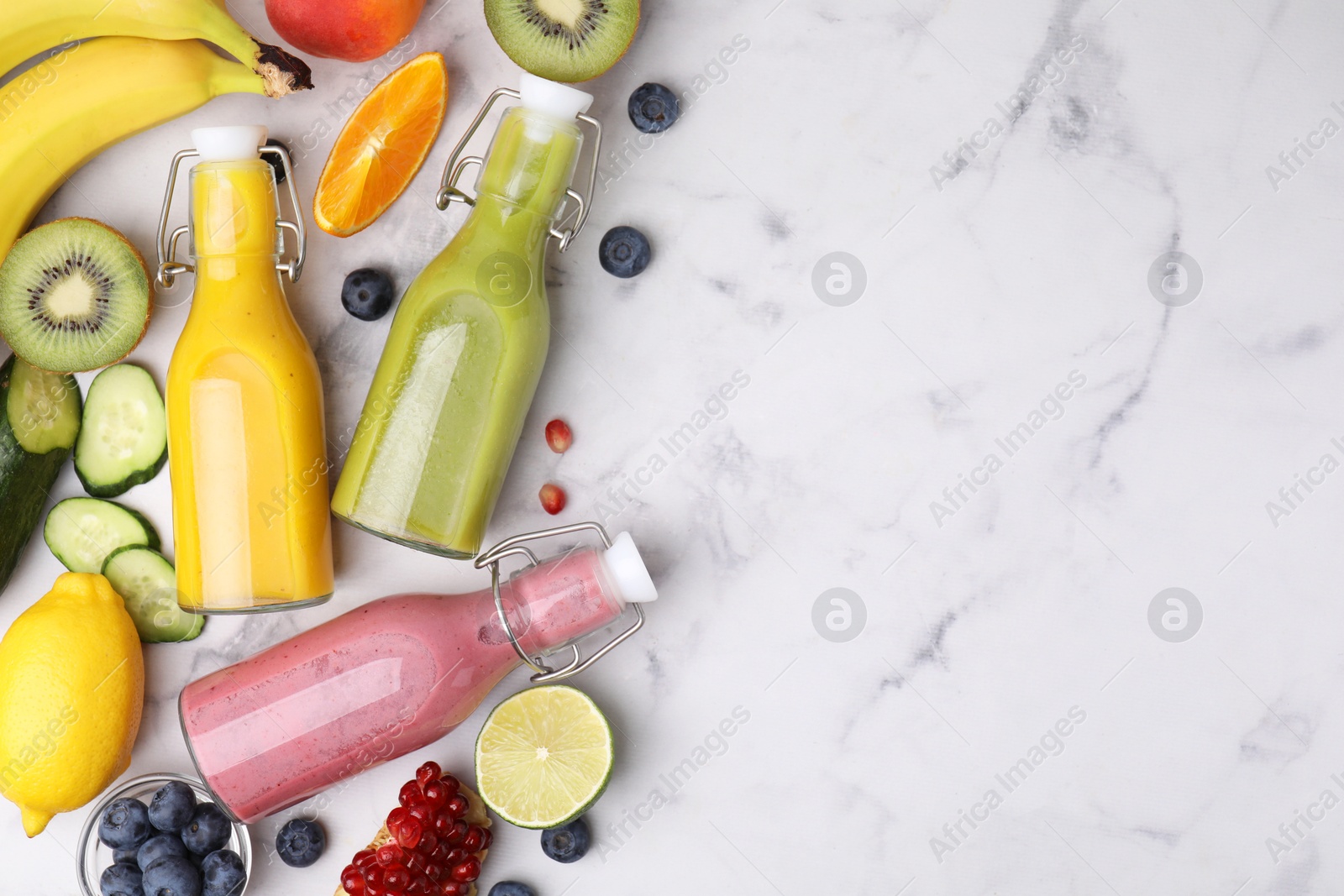 Photo of Glass bottles of tasty smoothies and different products on white marble table, flat lay. Space for text