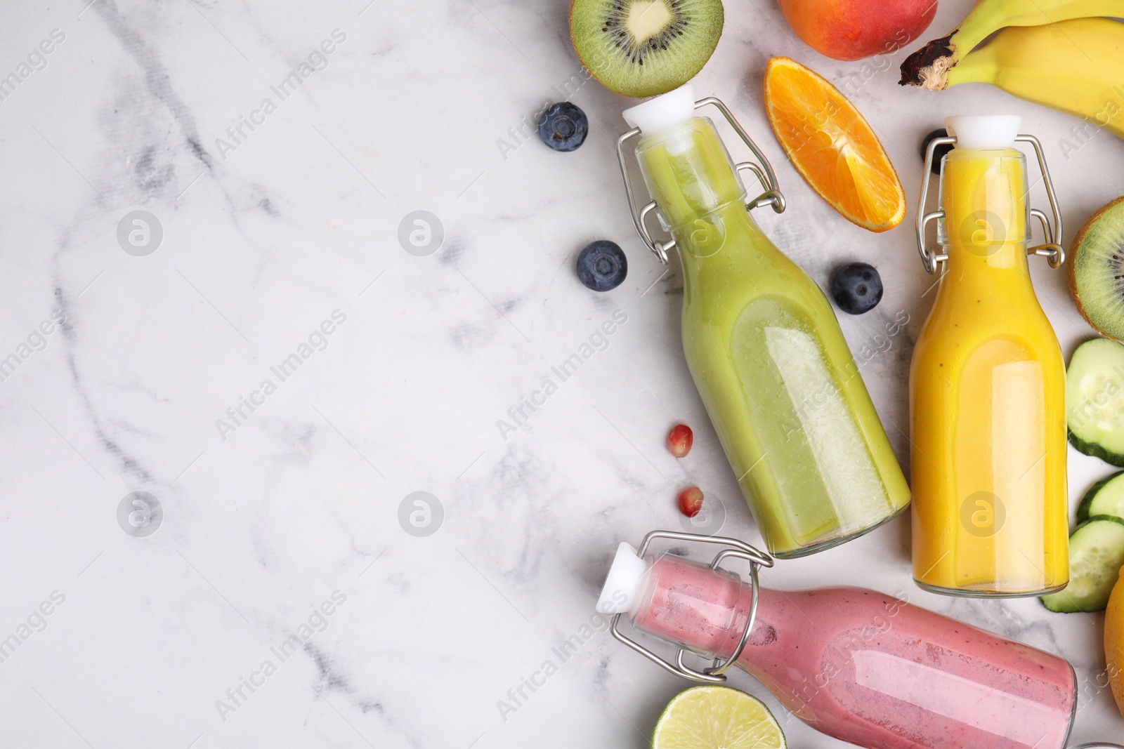 Photo of Glass bottles of tasty smoothies and different products on white marble table, flat lay. Space for text