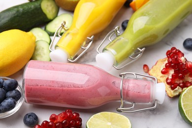 Glass bottles of tasty smoothies and different products on white marble table