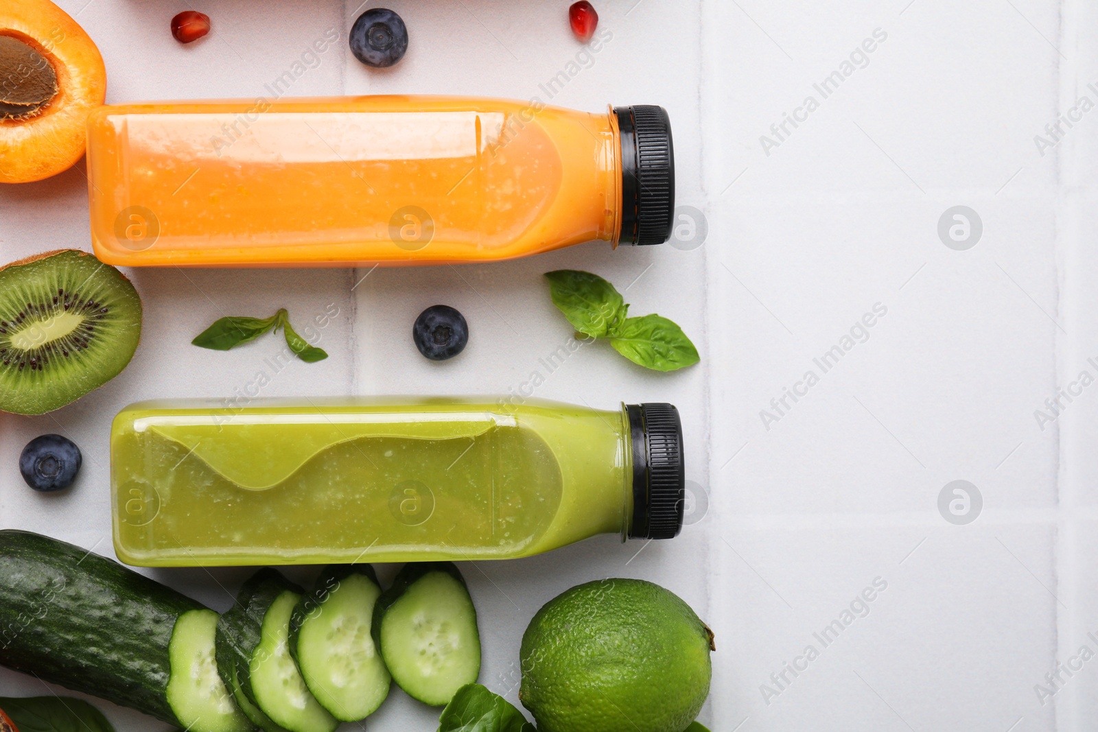 Photo of Glass bottles of tasty smoothies and different products on white tiled table, flat lay. Space for text