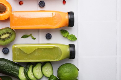 Glass bottles of tasty smoothies and different products on white tiled table, flat lay. Space for text