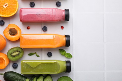 Photo of Glass bottles of tasty smoothies and different products on white tiled table, flat lay. Space for text