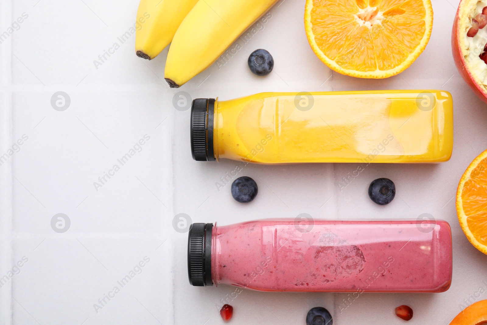 Photo of Glass bottles of tasty smoothies and different products on white tiled table, flat lay. Space for text