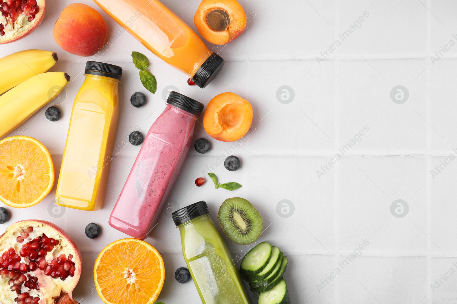 Photo of Glass bottles of tasty smoothies and different products on white tiled table, flat lay. Space for text