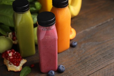 Glass bottles of tasty smoothies and different products on wooden table, closeup. Space for text