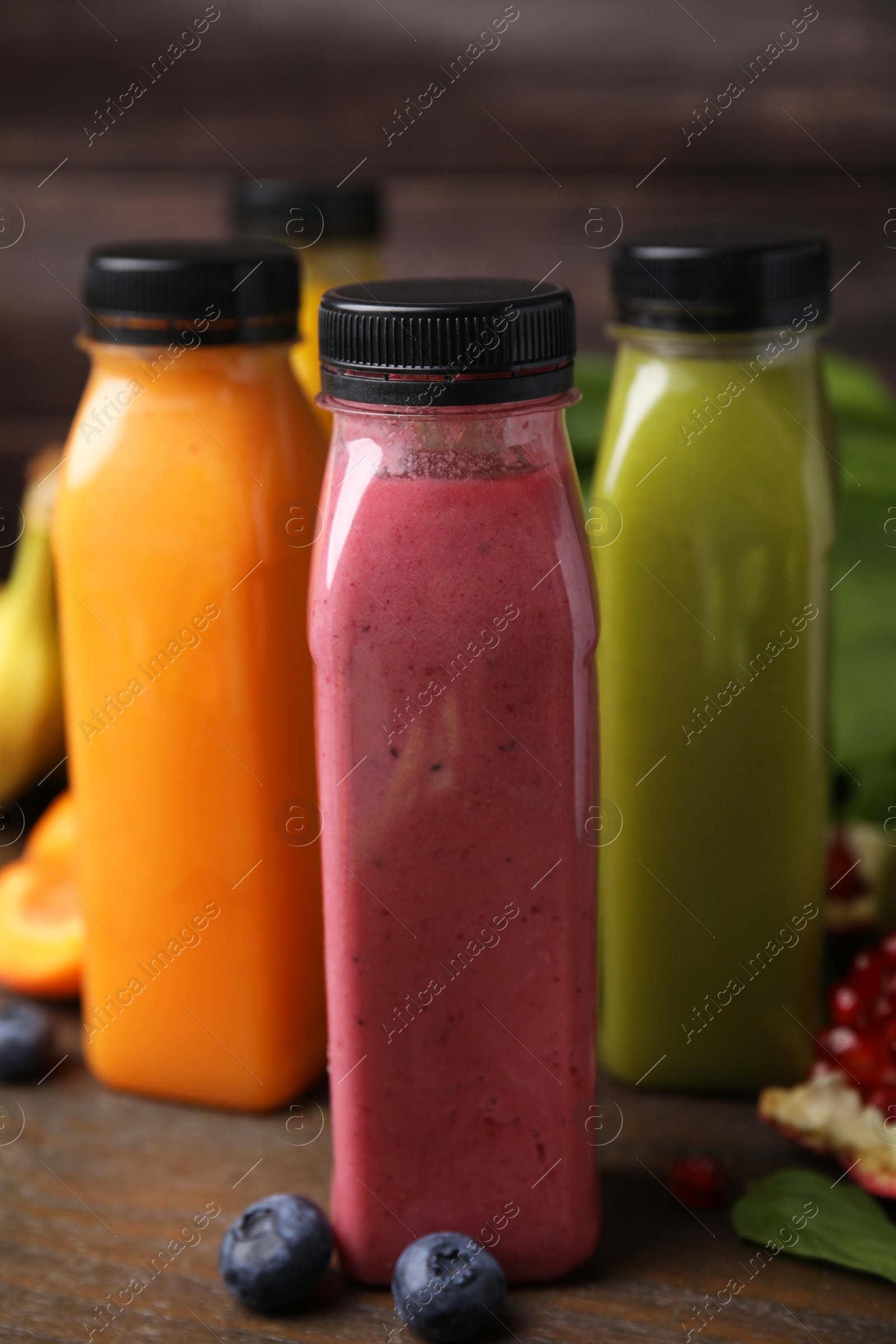 Photo of Glass bottles of tasty smoothies and different products on wooden table, closeup