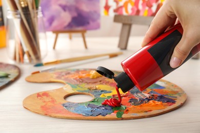 Photo of Woman mixing paints on palette at wooden table indoors, closeup