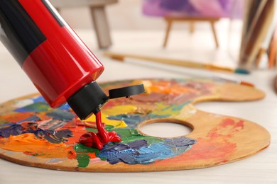 Photo of Squeezing red acrylic paint on palette at wooden table indoors, closeup