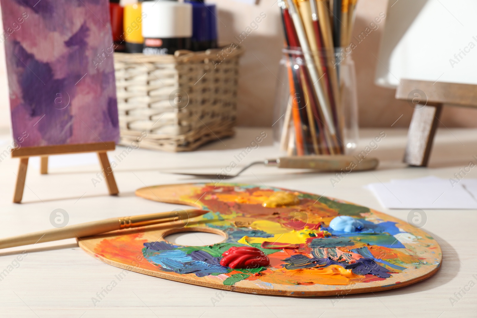 Photo of Artist's palette with mixed paints, brush and knife on wooden table