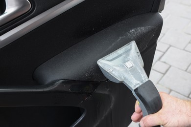 Photo of Man cleaning car door with vacuum cleaner outdoors, closeup