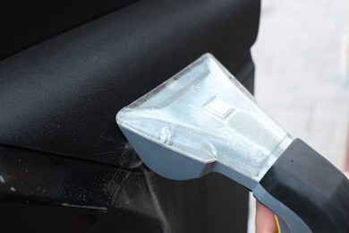 Photo of Man cleaning car door with vacuum cleaner outdoors, closeup