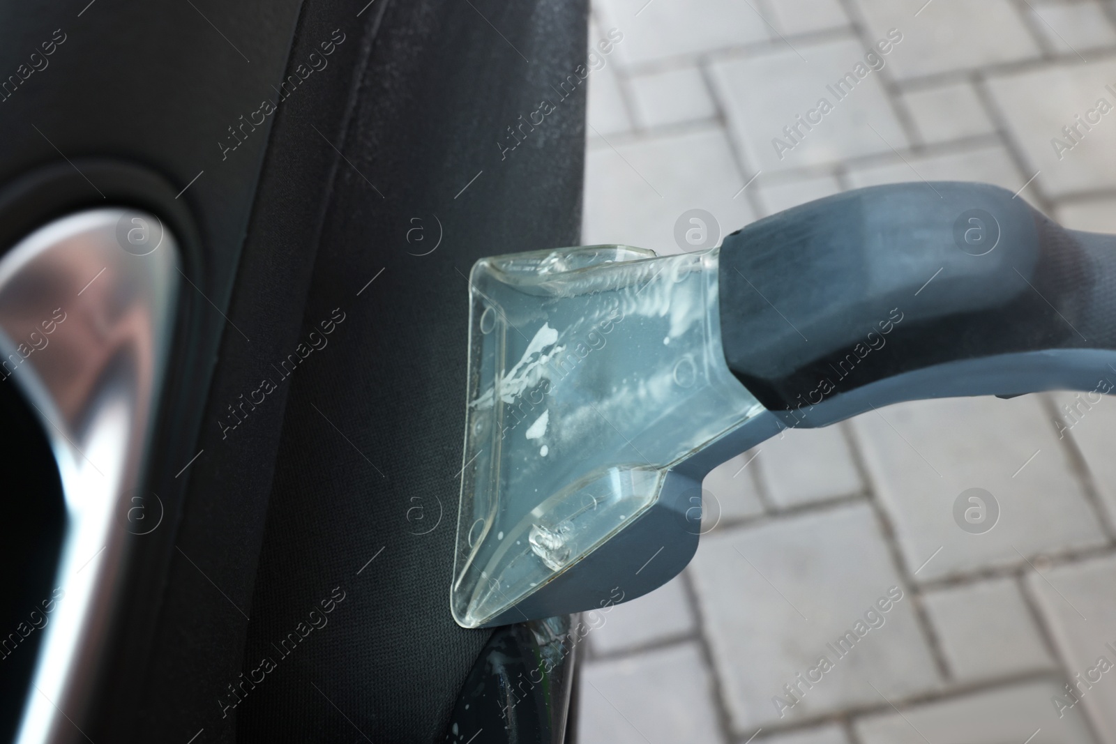 Photo of Man cleaning car door with vacuum cleaner outdoors, closeup