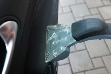 Photo of Man cleaning car door with vacuum cleaner outdoors, closeup