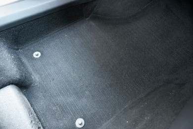 Photo of Black soft car floor mat in auto, closeup