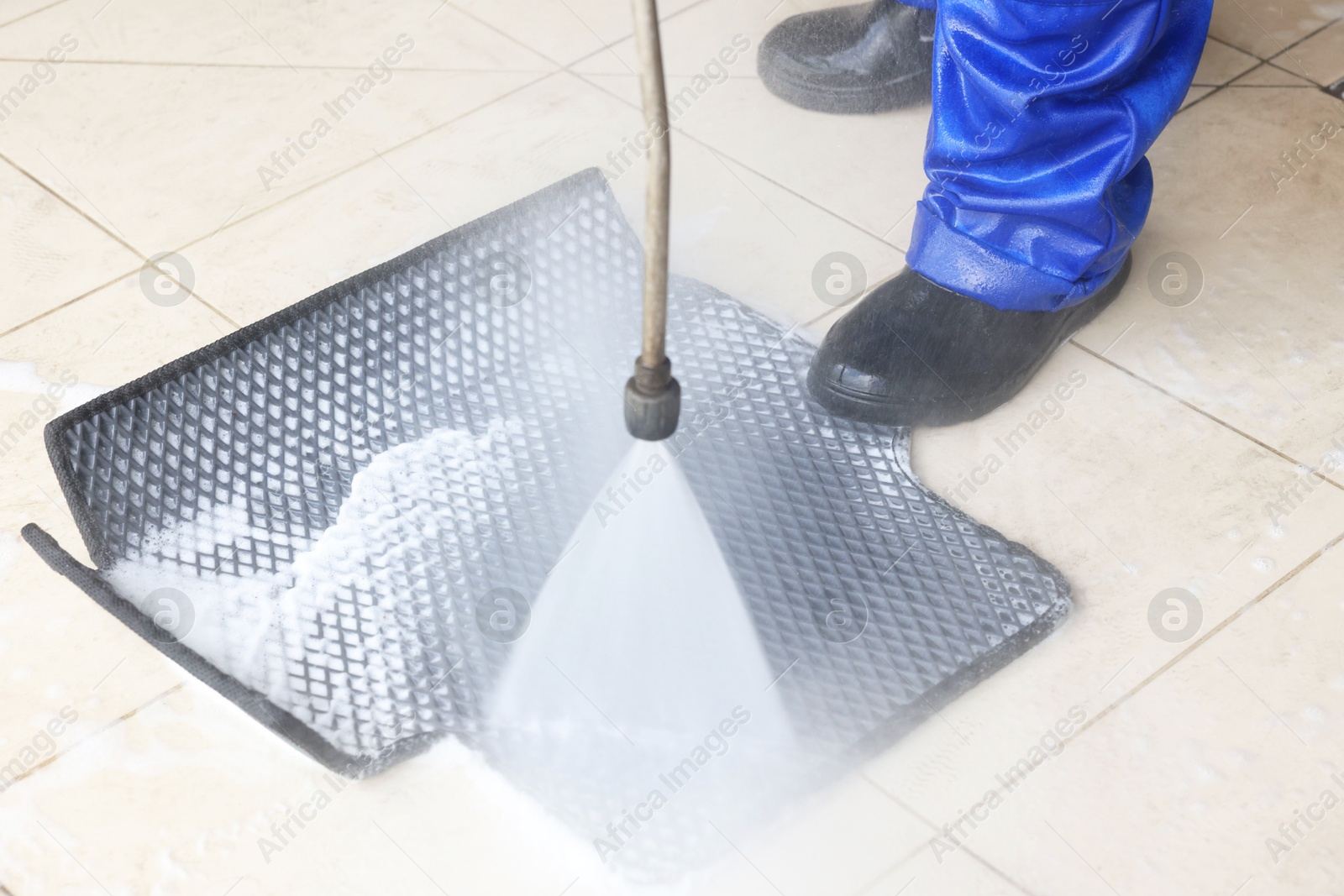 Photo of Man washing rubber car mat with high pressure water jet indoors, closeup