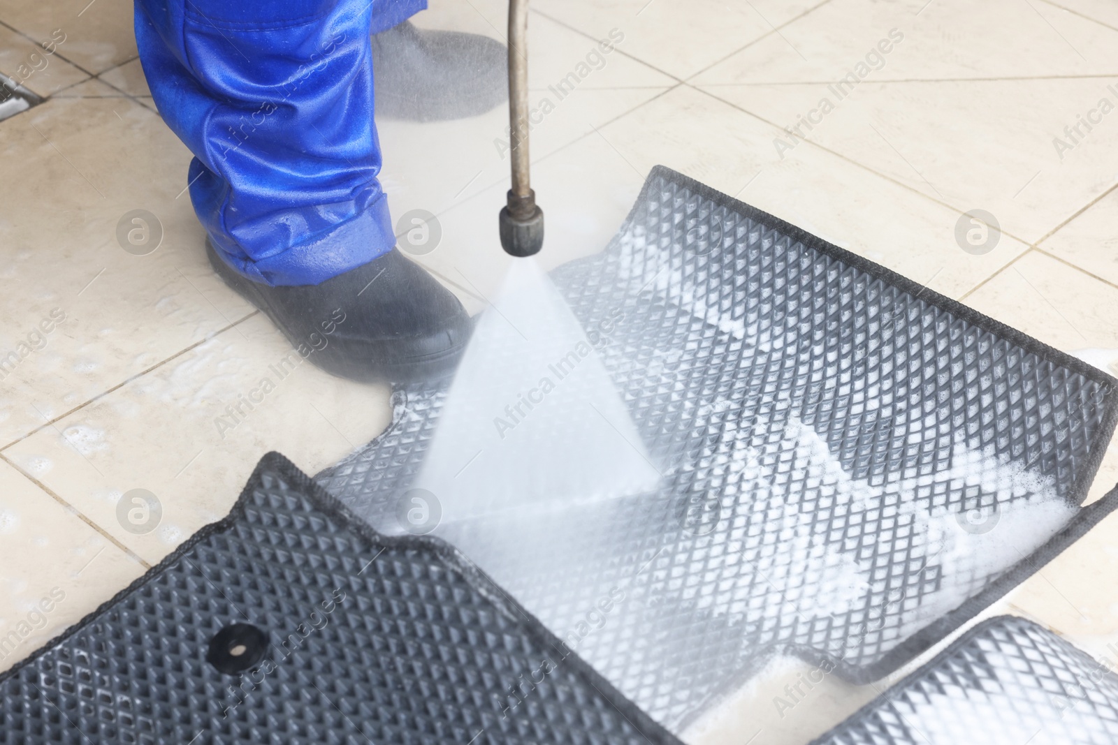 Photo of Man washing rubber car mats with high pressure water jet indoors, closeup