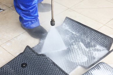 Photo of Man washing rubber car mats with high pressure water jet indoors, closeup