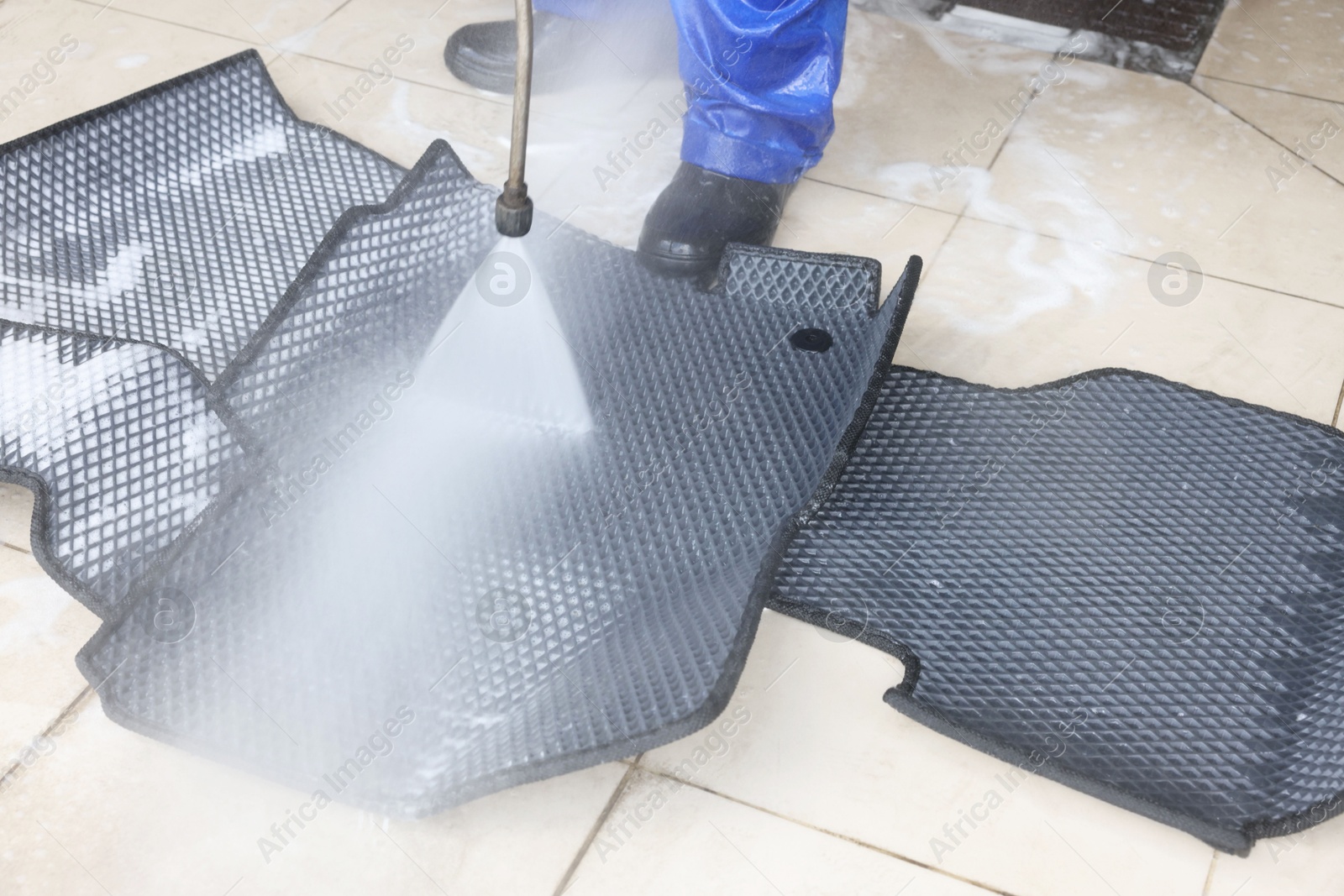 Photo of Man washing rubber car mats with high pressure water jet indoors, closeup