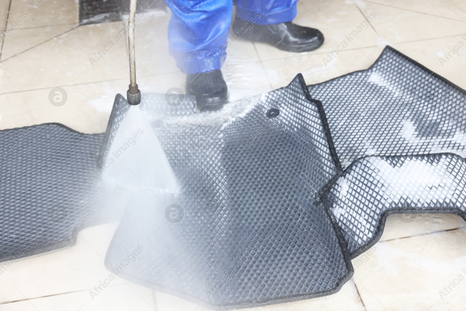 Photo of Man washing rubber car mats with high pressure water jet indoors, closeup