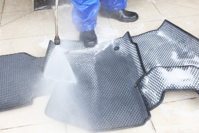 Photo of Man washing rubber car mats with high pressure water jet indoors, closeup