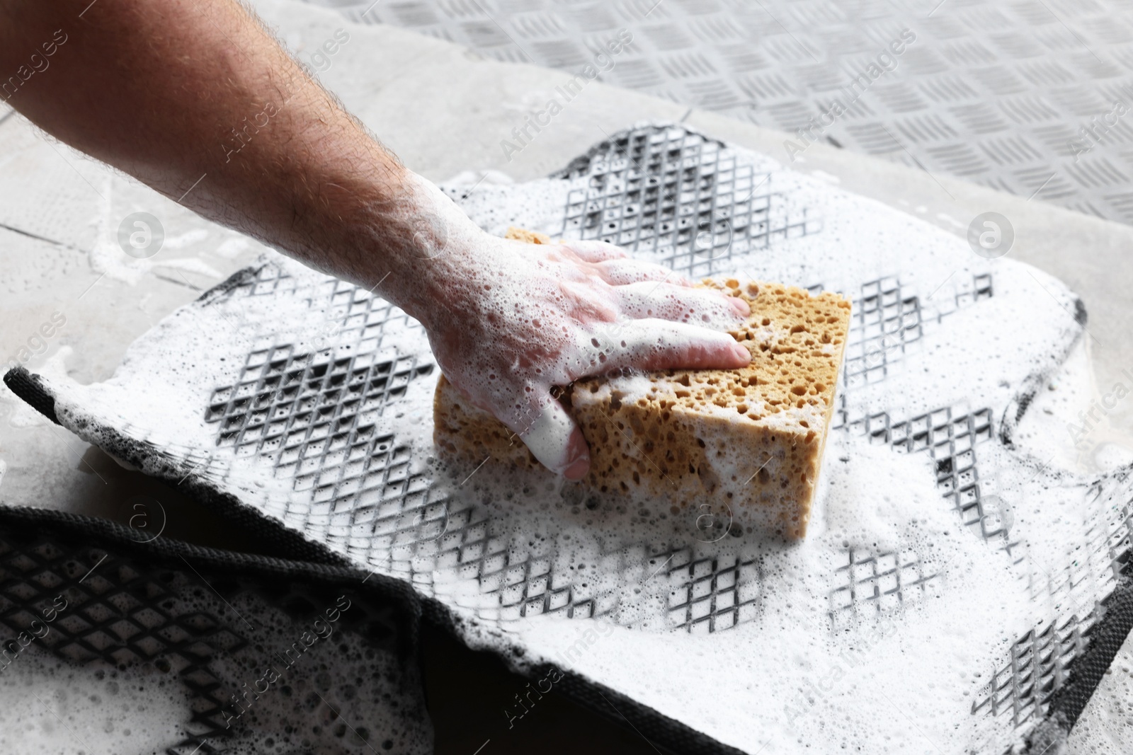 Photo of Man washing rubber car mat with sponge indoors, closeup