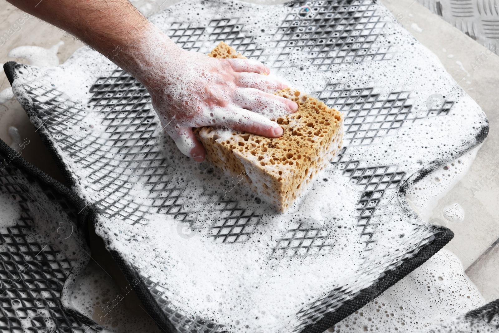 Photo of Man washing rubber car mat with sponge indoors, closeup