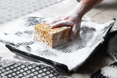 Photo of Man washing rubber car mat with sponge indoors, closeup