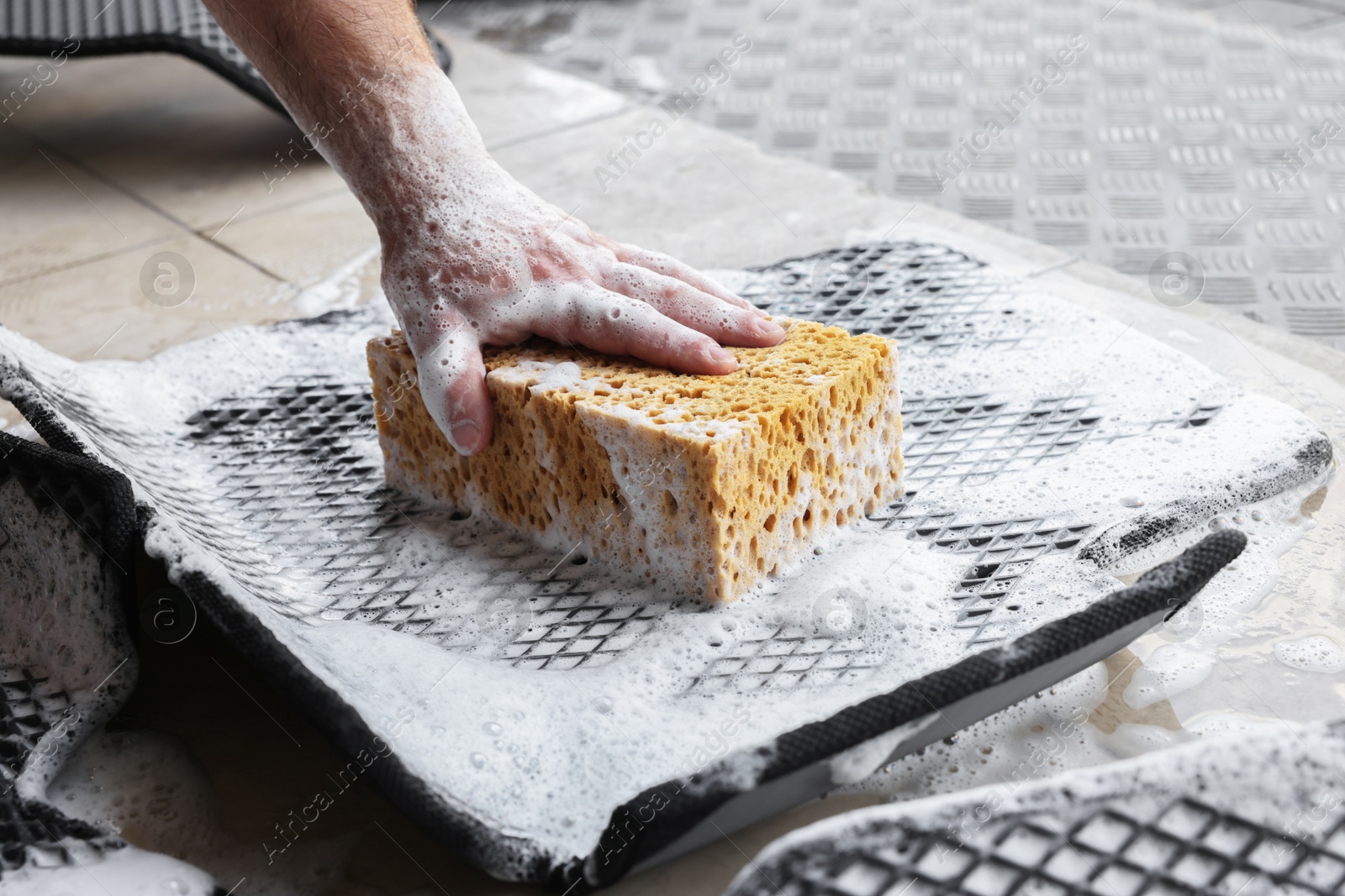 Photo of Man washing rubber car mat with sponge indoors, closeup