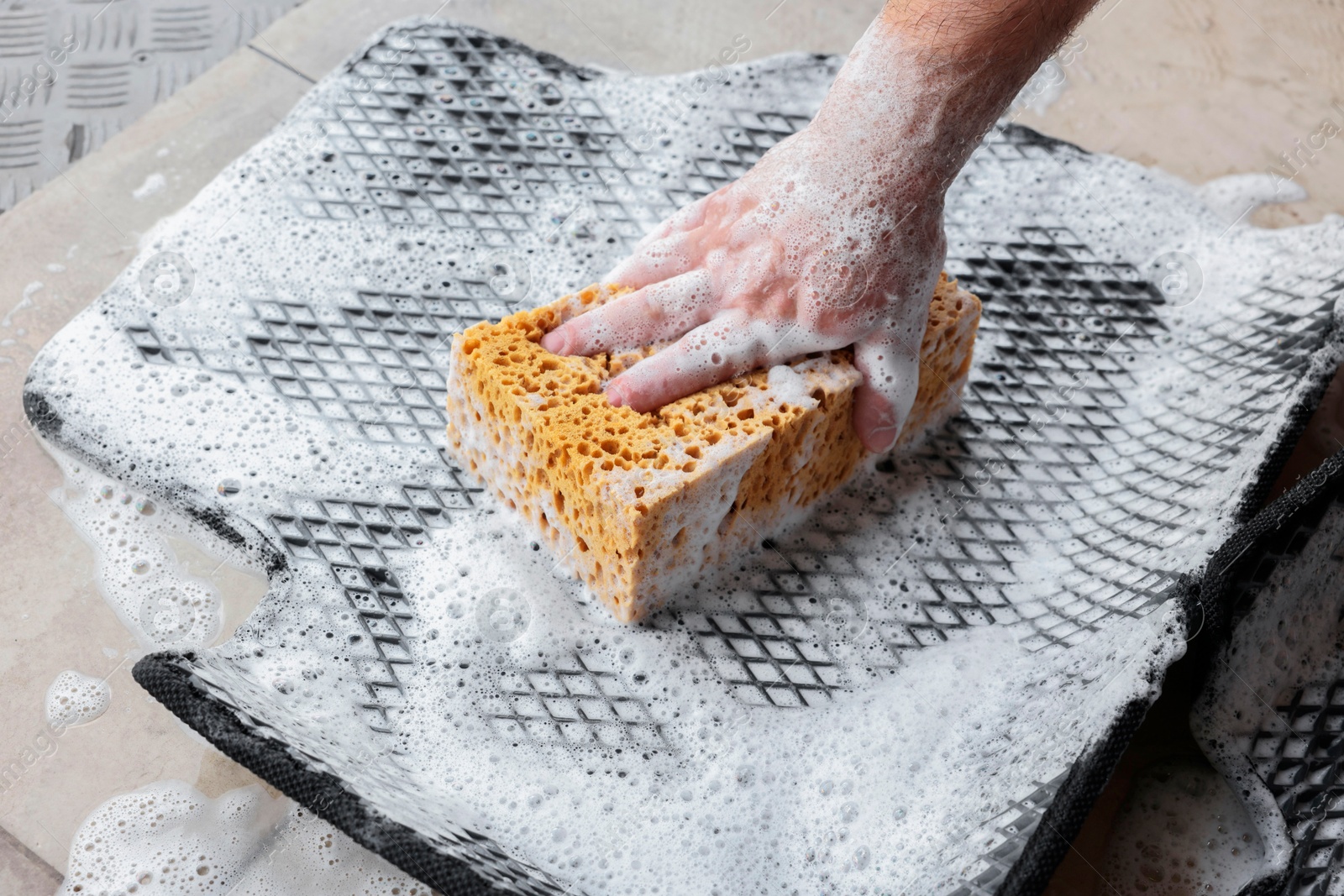 Photo of Man washing rubber car mat with sponge indoors, closeup