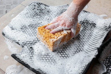 Photo of Man washing rubber car mat with sponge indoors, closeup