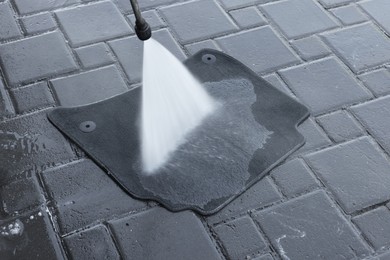 Photo of Washing car mat with high pressure water jet outdoors, closeup