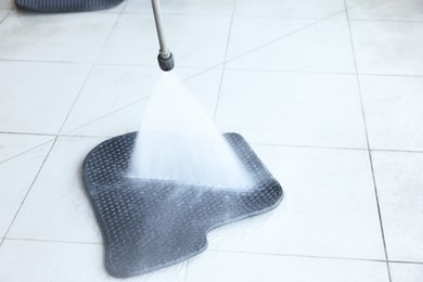 Photo of Washing rubber car mat with high pressure water jet indoors, closeup