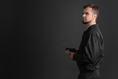 Security guard in uniform with gun on black background, space for text