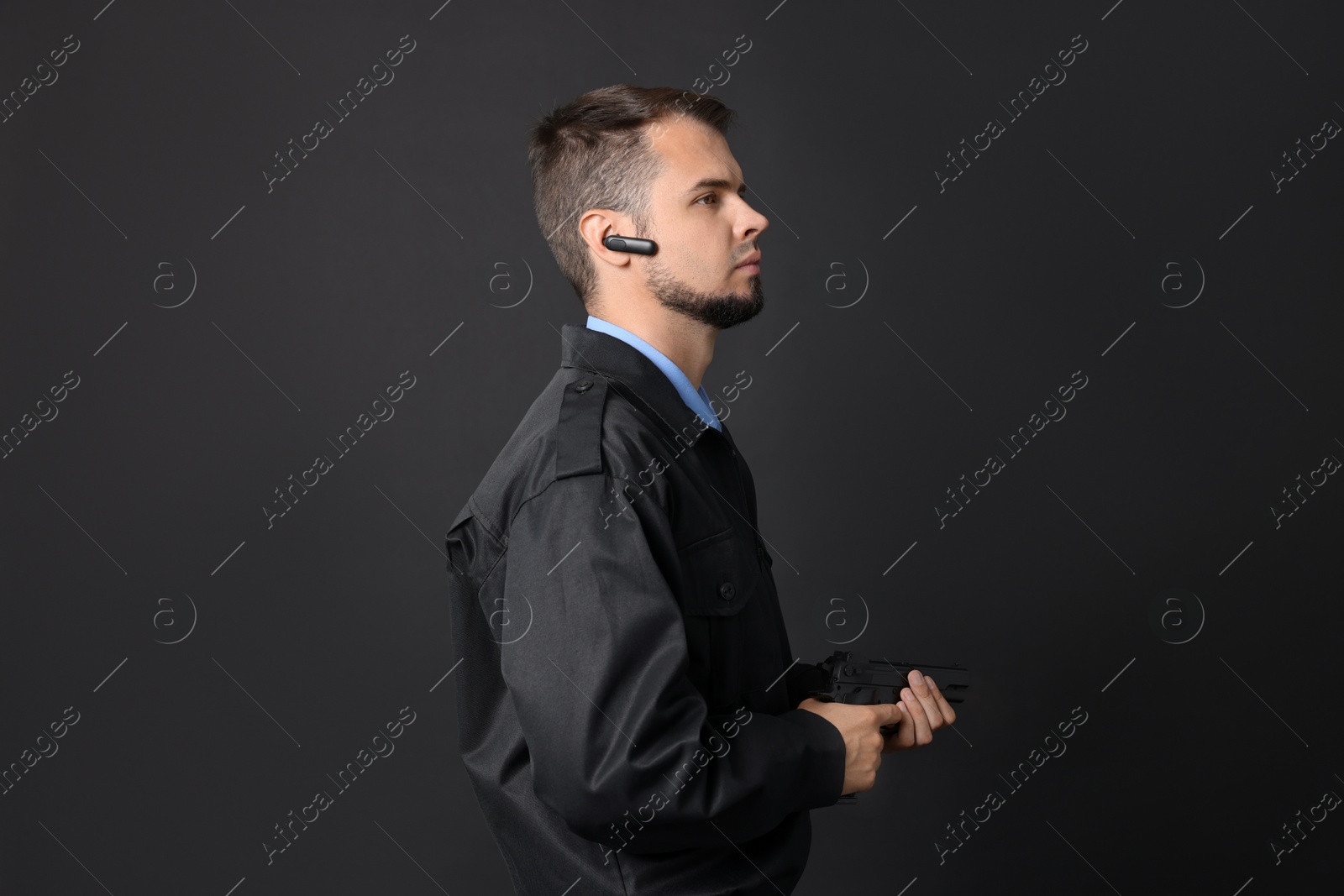 Photo of Security guard in uniform with earpiece and gun on black background