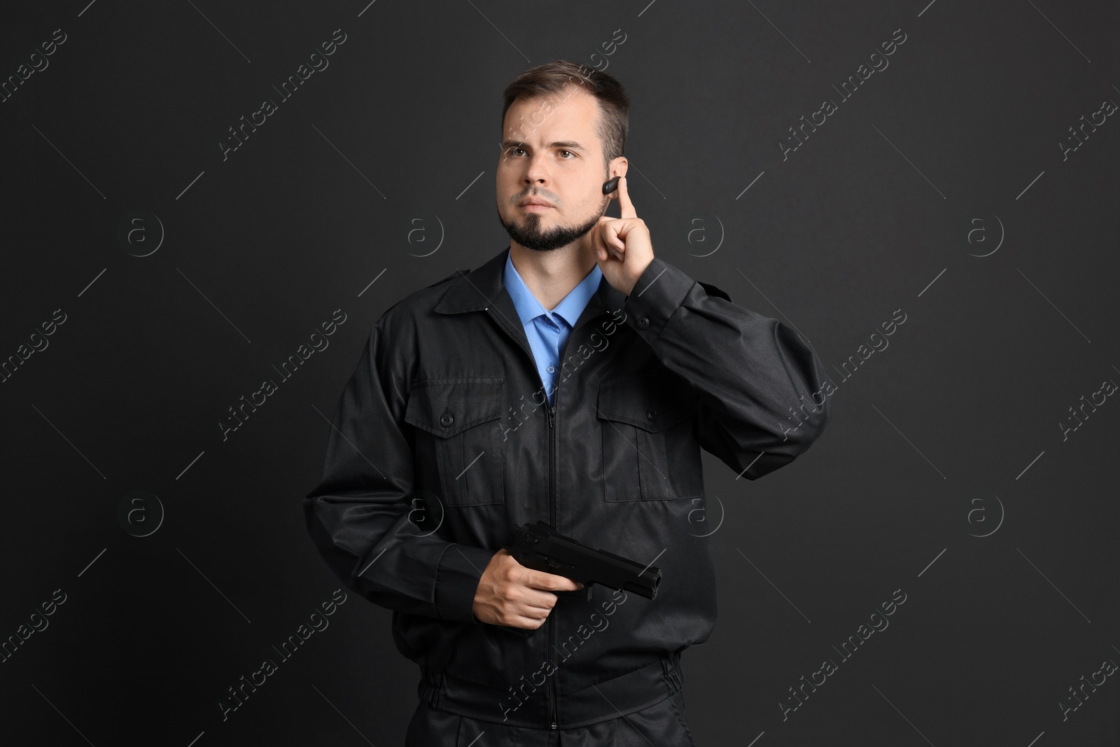 Photo of Security guard in uniform with earpiece and gun on black background