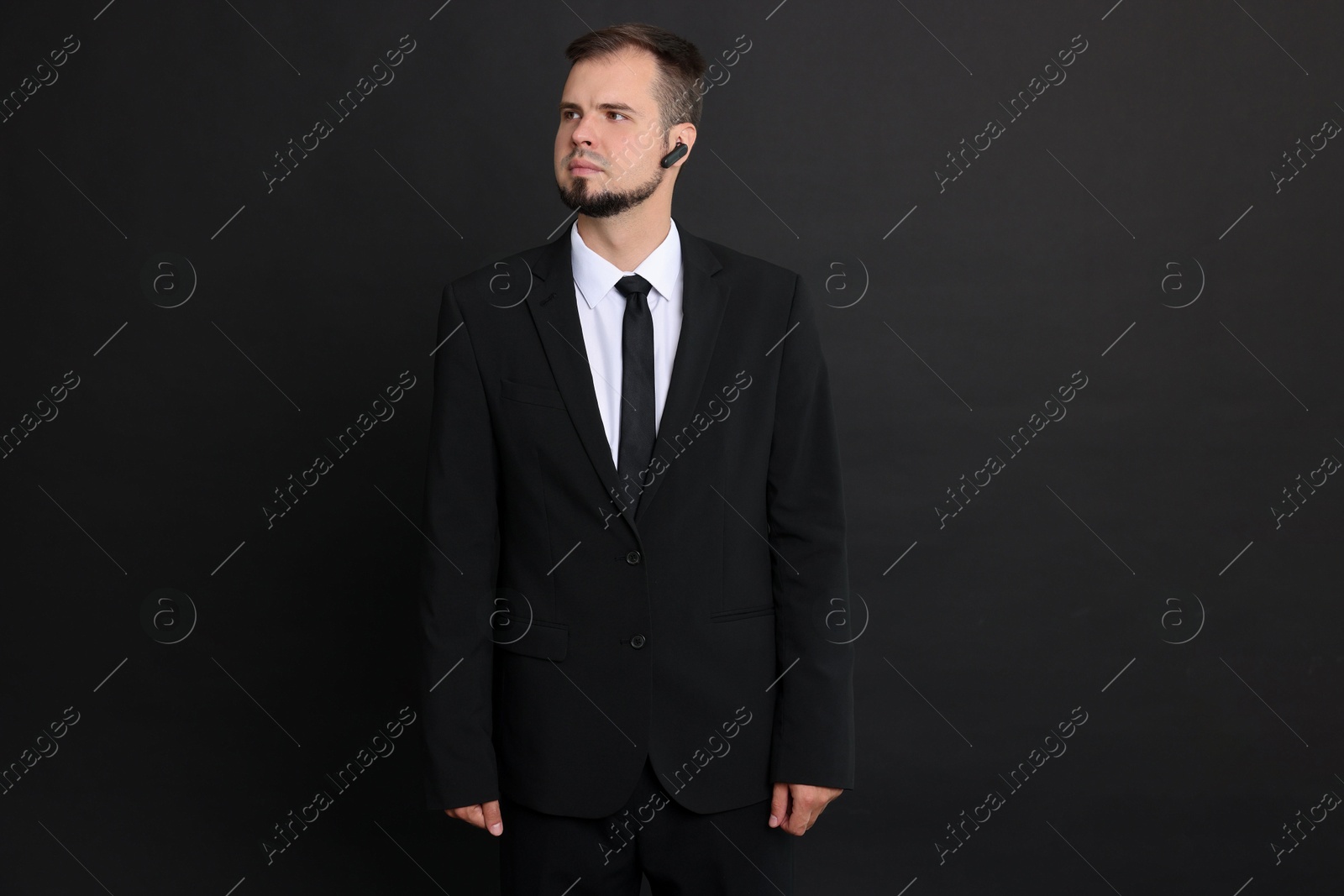 Photo of Young bodyguard in suit with earpiece on black background