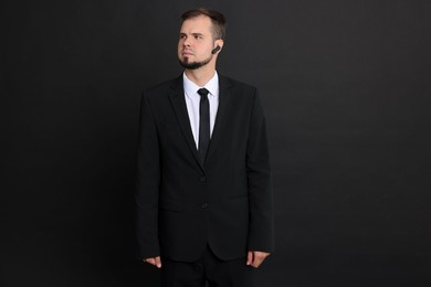 Photo of Young bodyguard in suit with earpiece on black background