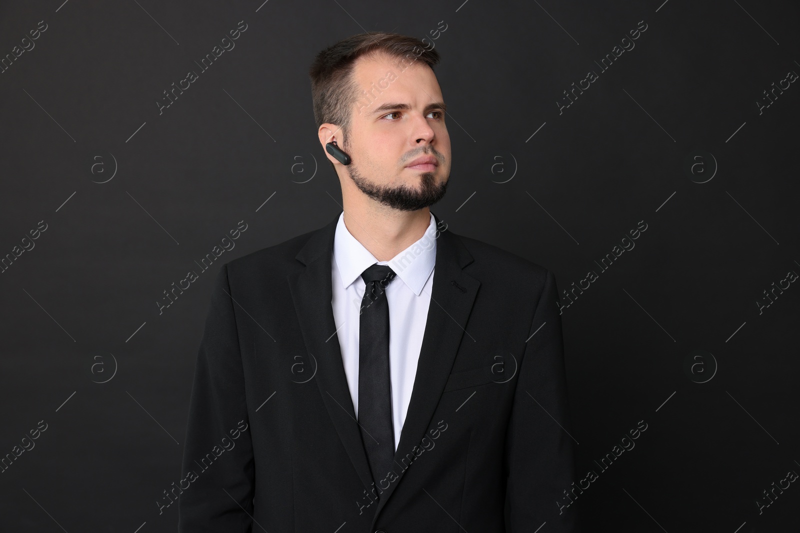 Photo of Young bodyguard in suit with earpiece on black background