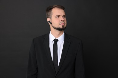 Young bodyguard in suit with earpiece on black background