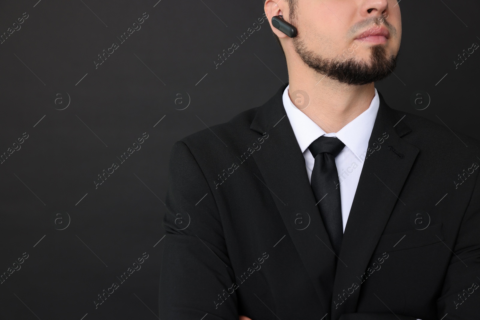 Photo of Young bodyguard in suit with earpiece on black background, closeup. Space for text