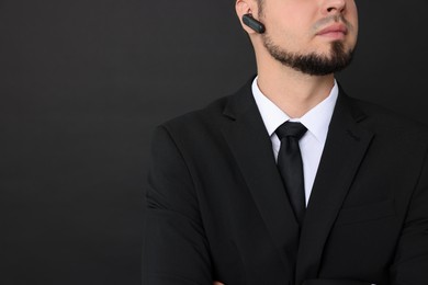 Young bodyguard in suit with earpiece on black background, closeup. Space for text