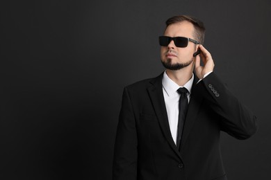 Photo of Young bodyguard in suit with sunglasses on black background, space for text