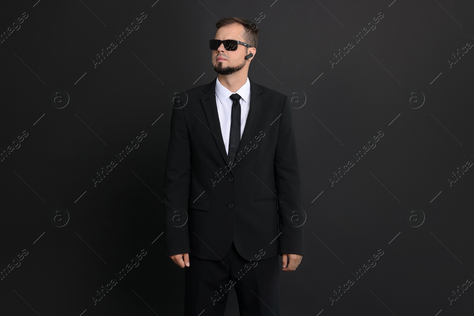 Photo of Young bodyguard in suit with sunglasses on black background