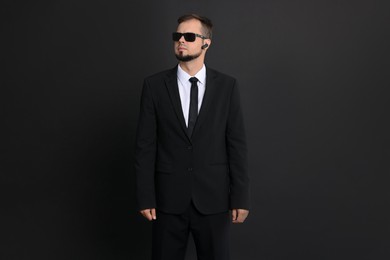 Photo of Young bodyguard in suit with sunglasses on black background