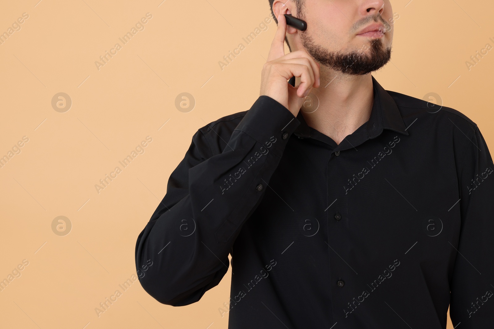 Photo of Young bodyguard with earpiece on beige background, closeup