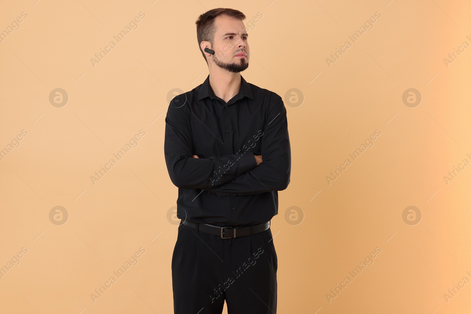 Photo of Young bodyguard with earpiece on beige background