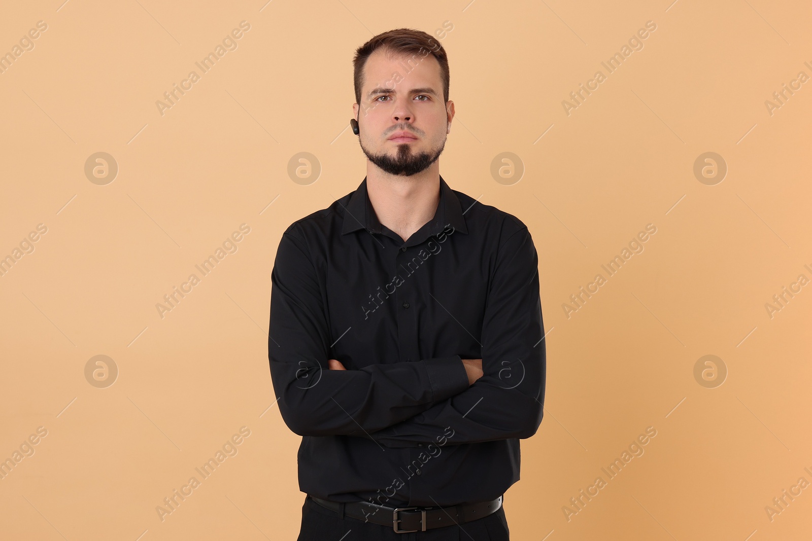 Photo of Young bodyguard with earpiece on beige background