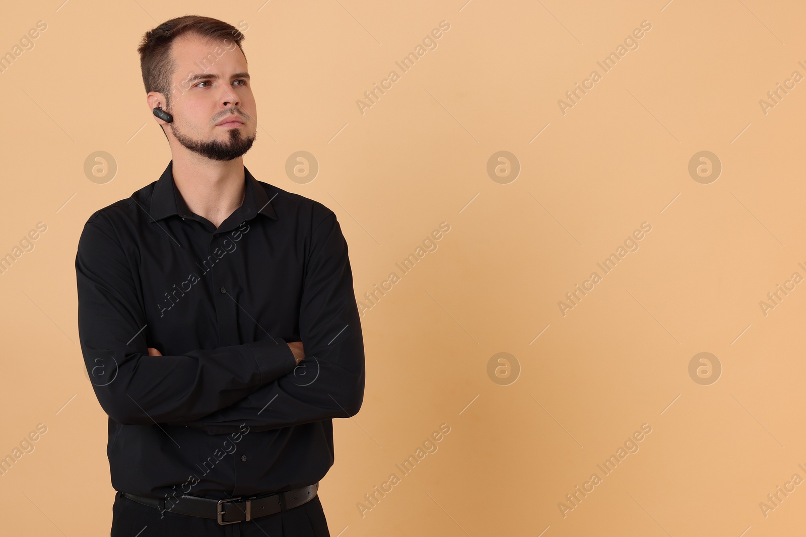 Photo of Young bodyguard with earpiece on beige background, space for text