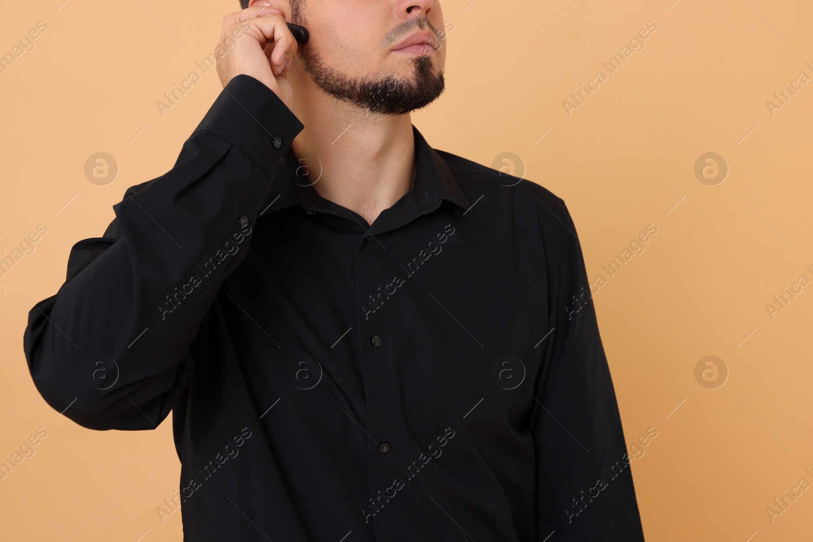 Photo of Young bodyguard with earpiece on beige background, closeup