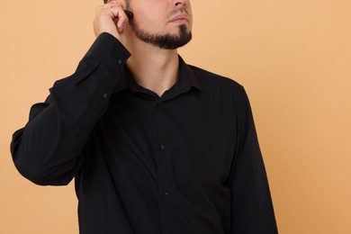 Photo of Young bodyguard with earpiece on beige background, closeup